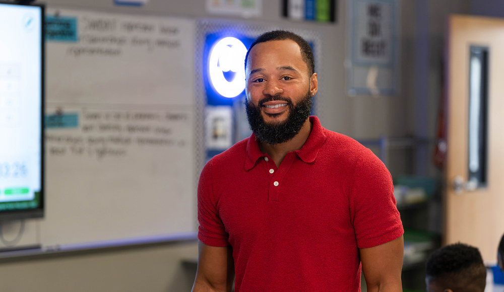 African American man with beard wearing red polo standing in classroom