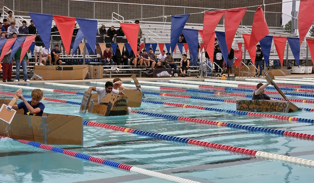 teen boys in cardboard boats racing in a swimming pool