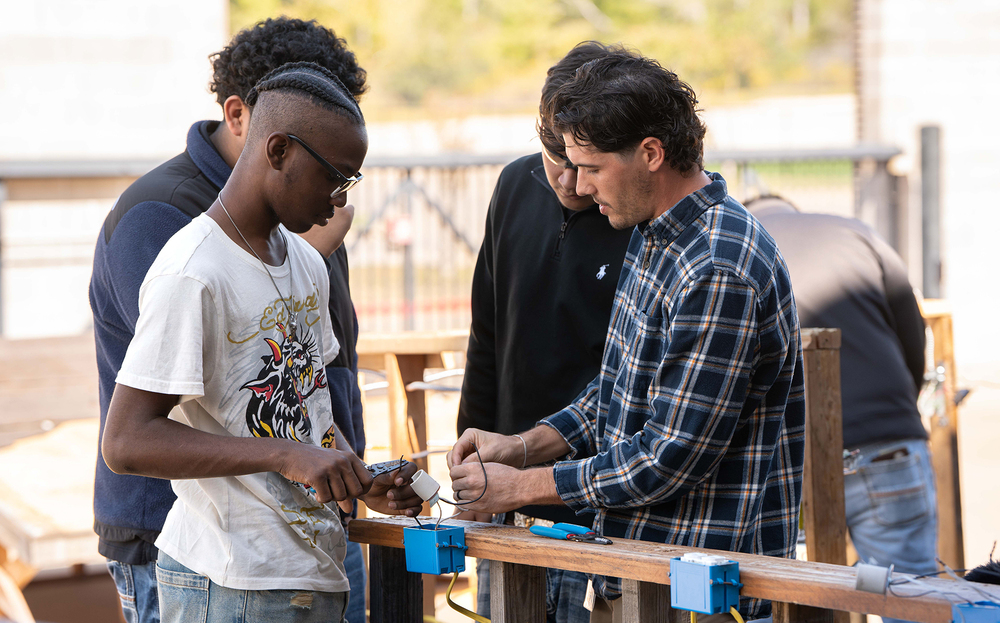 teen boys and man working on electrical wiring along 2x4