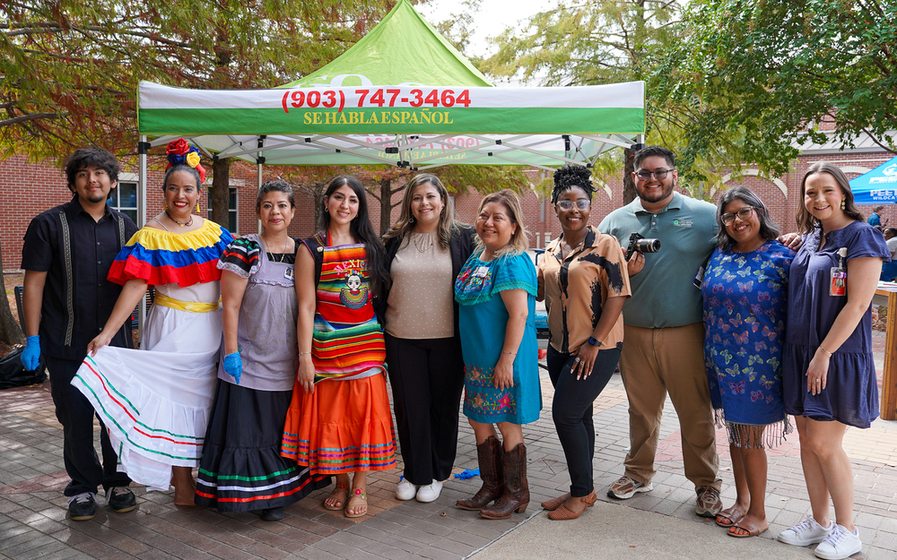 men and women standing in courtyard outside school. Some are dressed in traditional Hispanic attire.