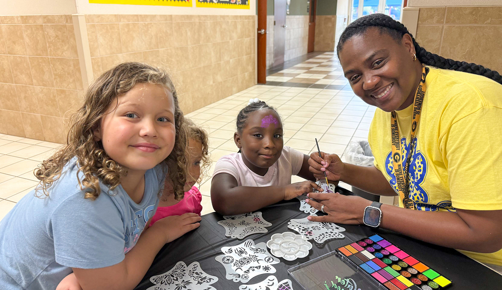 young girls at table picking out design for woman to paint their faces