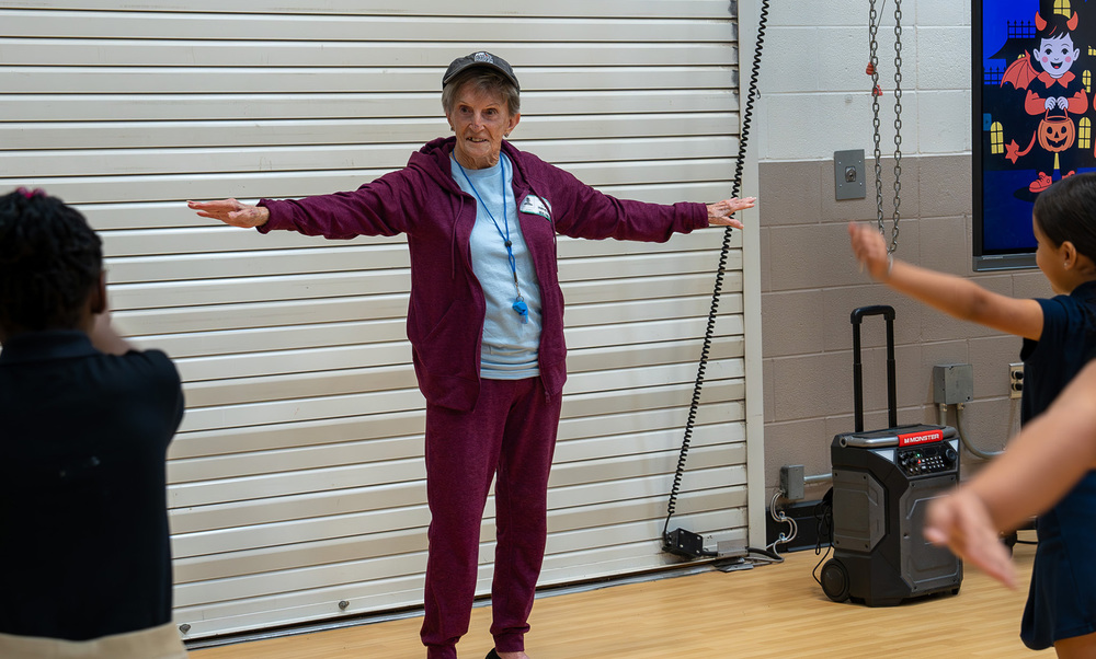 elderly woman in maroon tracksuit with her arms outstretched