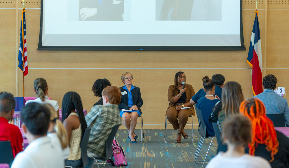 high school students in chairs listening to two women at front of room speaking