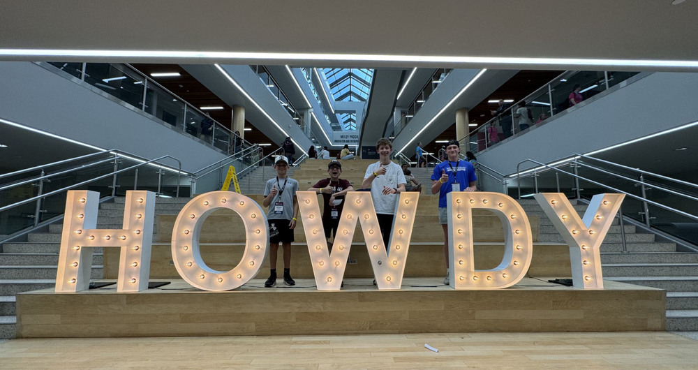 four teen boys standing behind a HOWDY sign