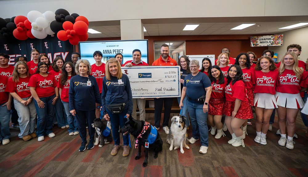 teens, adults, and puppies gathered around a giant check