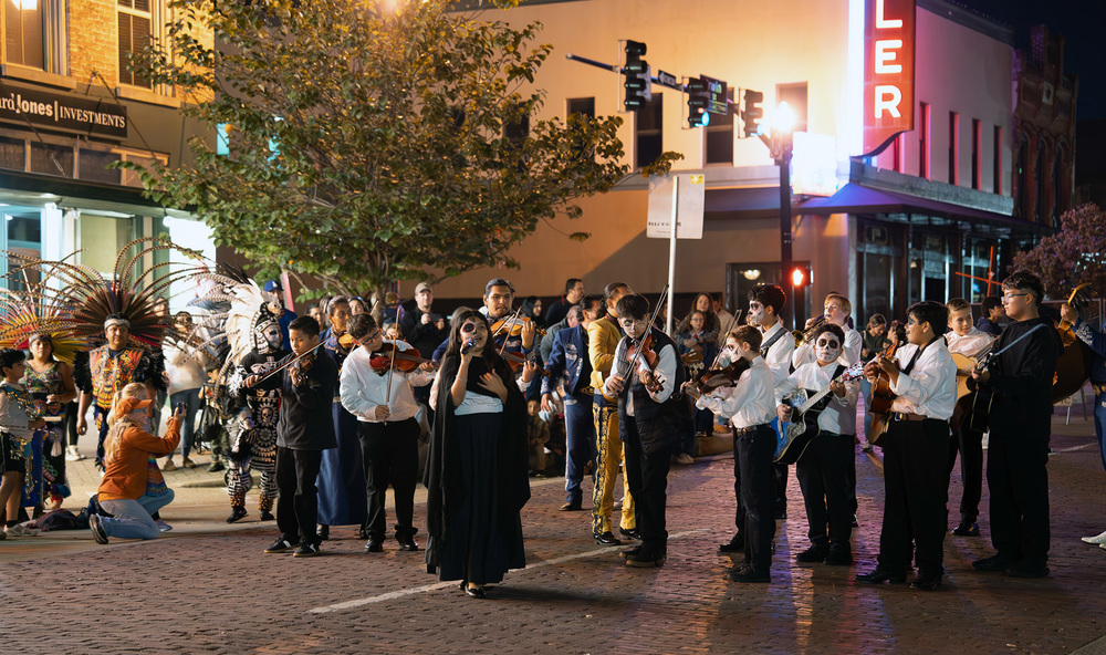 students in mariachi band playing instruments on brick street