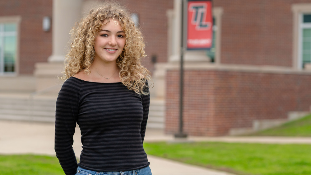 teen girl with curly blonde hair standing outside school building
