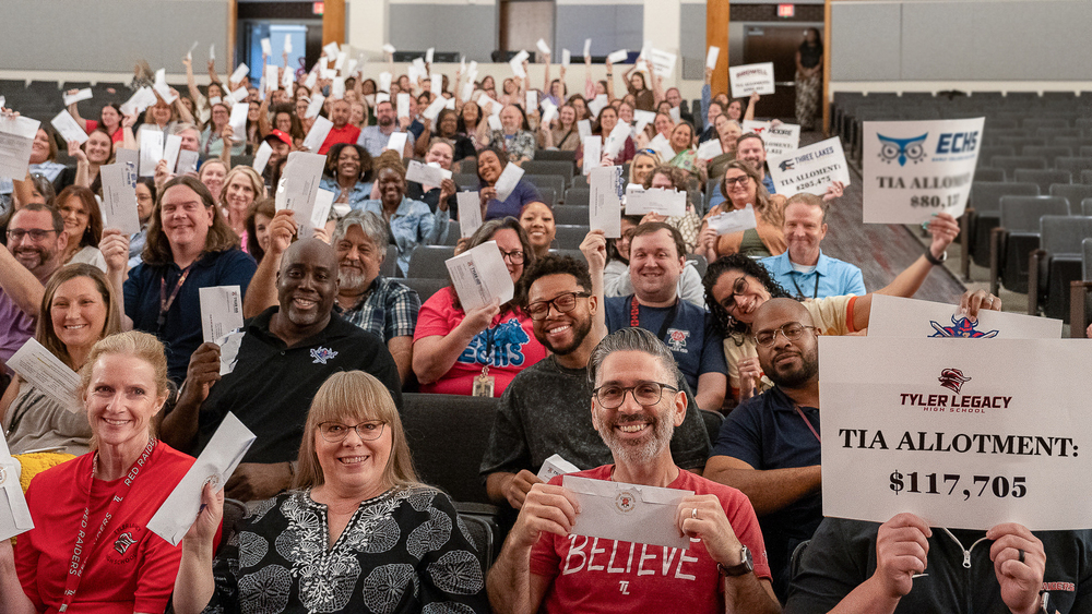 crowd of men and women sitting in chairs holding up envelopes