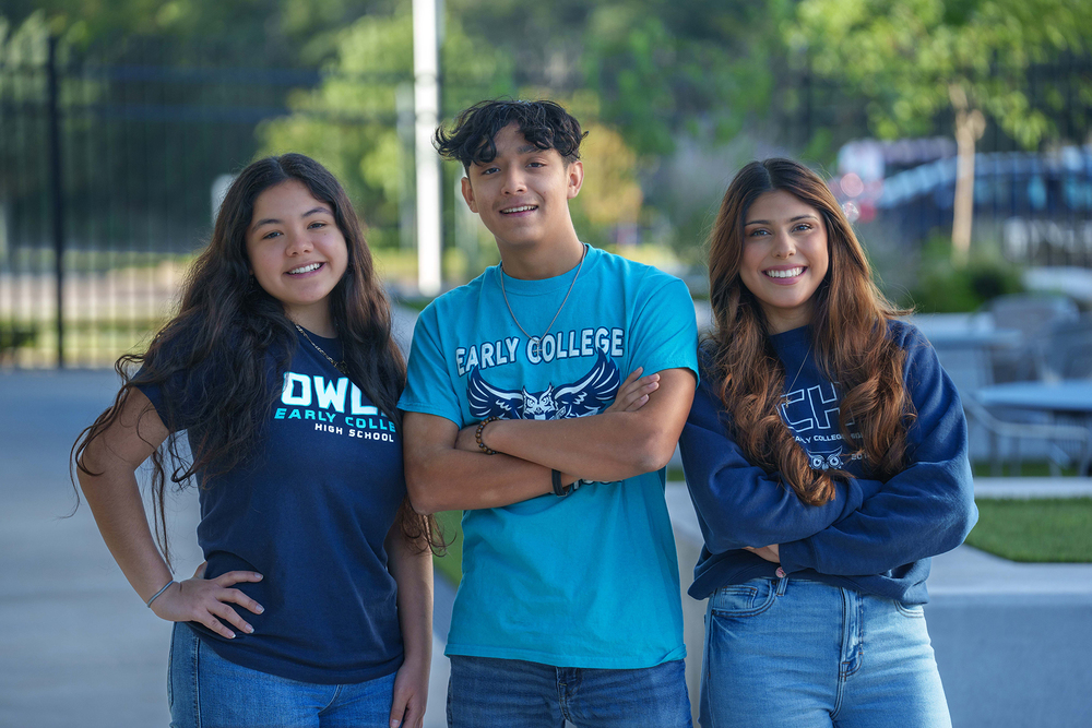 three teens wearing blue shirts standing on a sidewalk