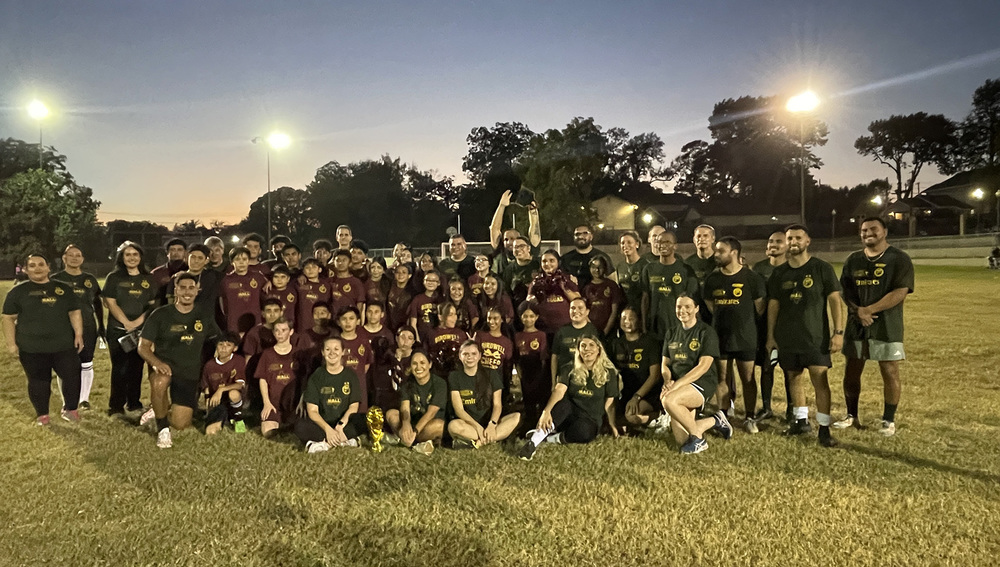 adults and kids wearing soccer jerseys in a group on the grass