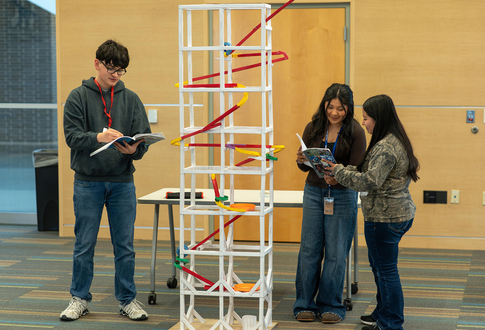 teen boy and two girls standing next to roller coaster made from paper and tape
