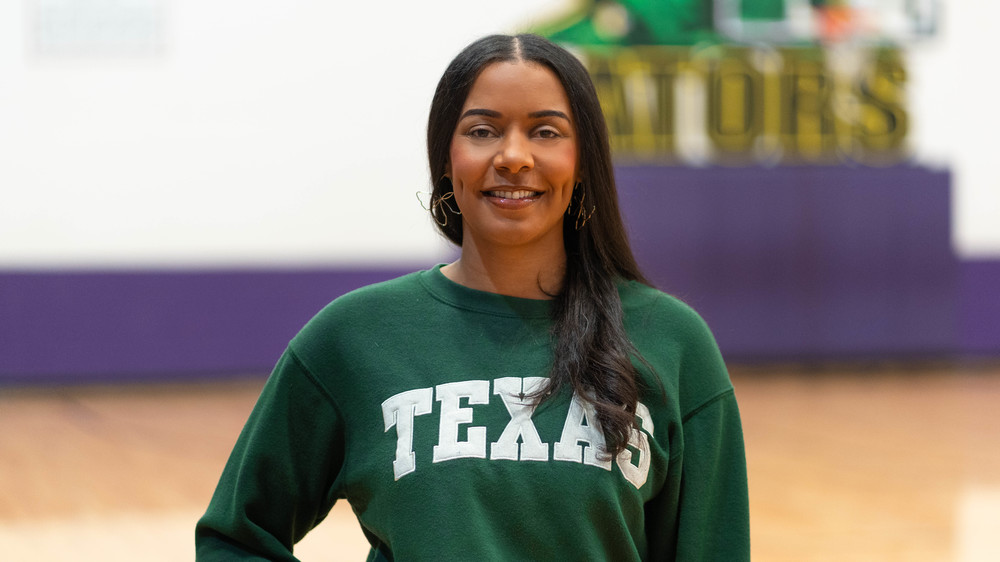 woman with long dark hair wearing green TEXAS sweatshirt standing in sym