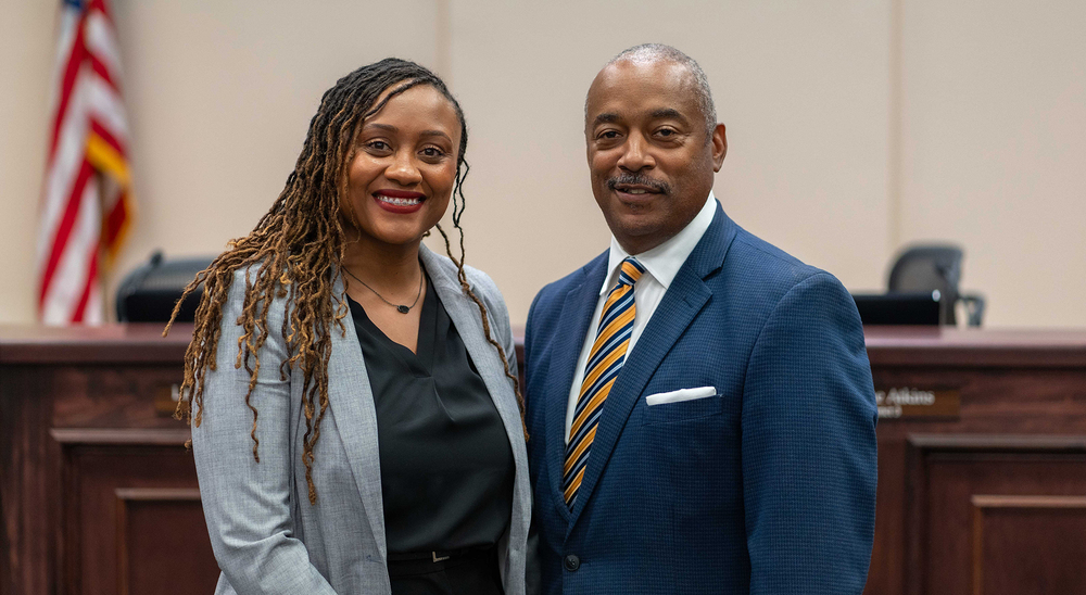 African American man and woman standing next to each other in front of wood desk