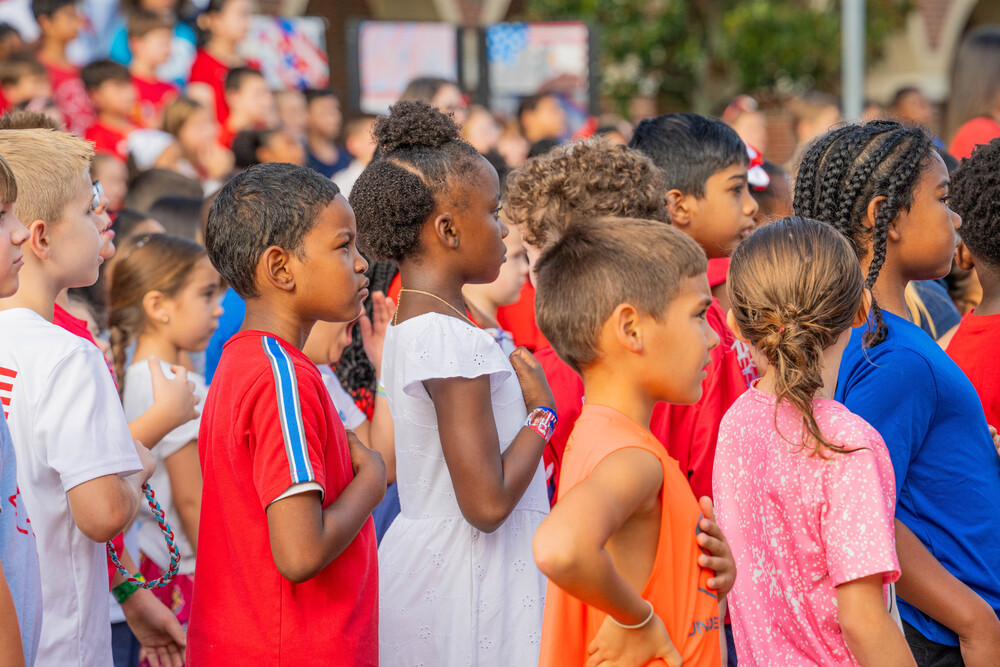 elementary age students standing together with their hands on their hearts saying the Pledge of Allegiance