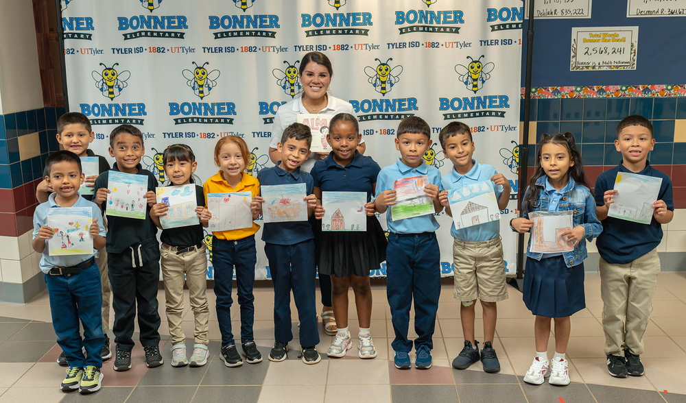 group of elementary age boys and girls holding up drawings of their families