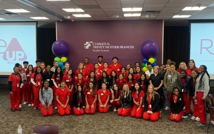 teens in red scrubs grouped in front of CHRISTUS Trinity Mother Frances Health System sign