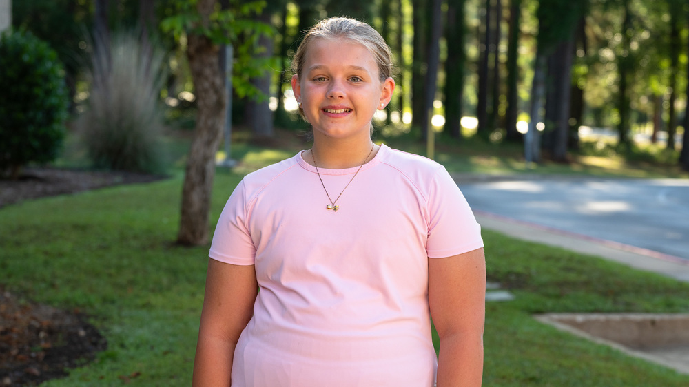 elementary age girl wearing pink t-shirt standing in grassy yard