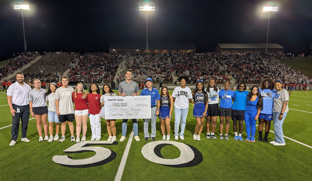 adults and teens standing on 50 yeard line holding giant check