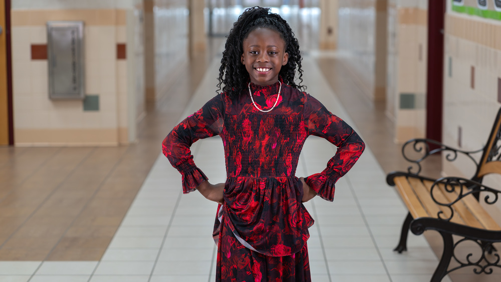elementary age girl standing in school hallway with hands on her hips