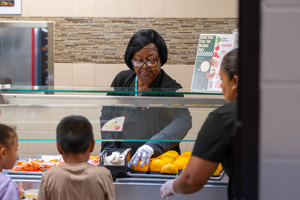 woman passing out oranges to kids in cafeteria line