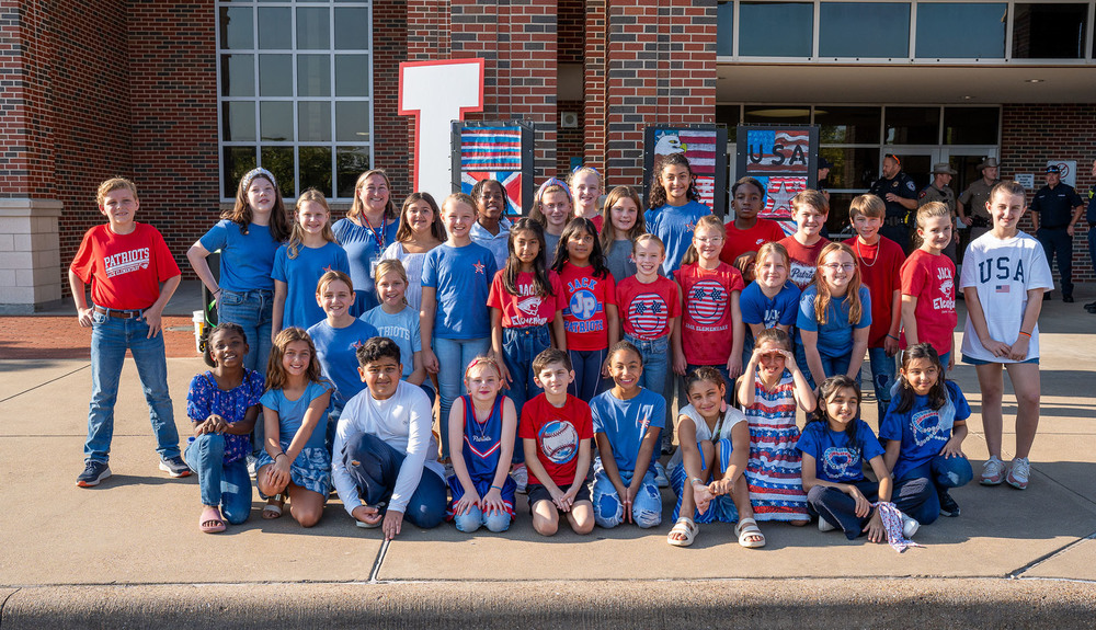 elementary age kids dressed in red, white, and blue in front of a school