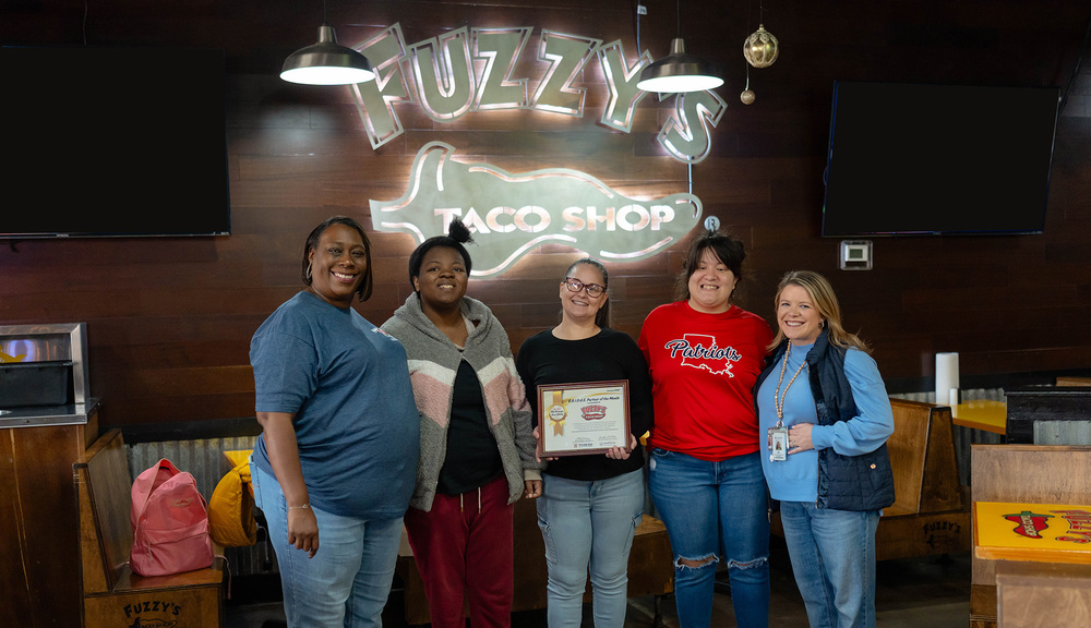 women and teen girls in front of Fuzzy's Taco sign holding a certificate