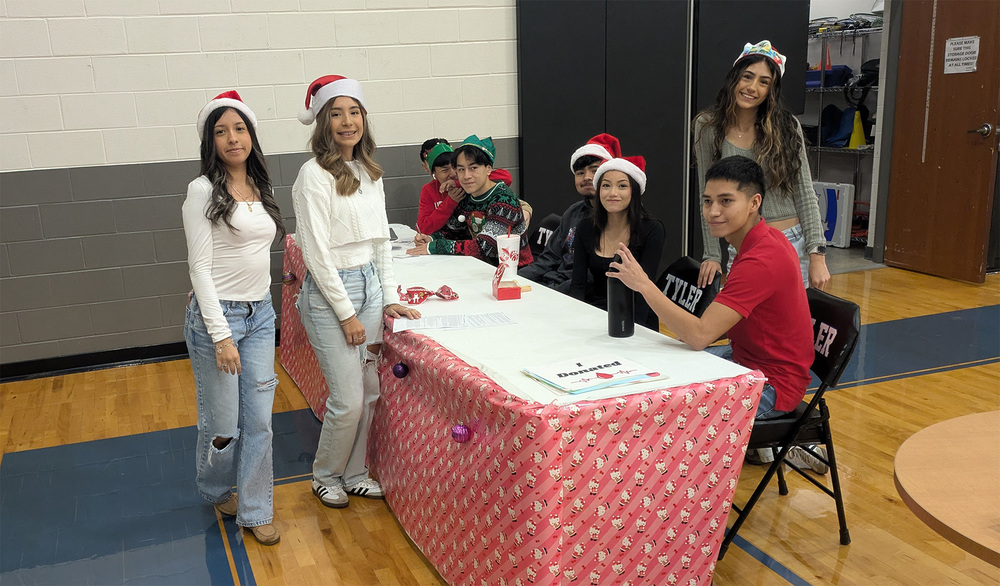 teens wearing Santa hats sitting at a table in a gym