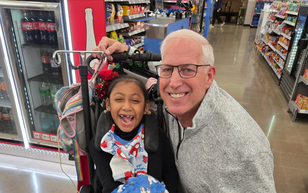 young child in wheelchair with man next to her and both smiling big