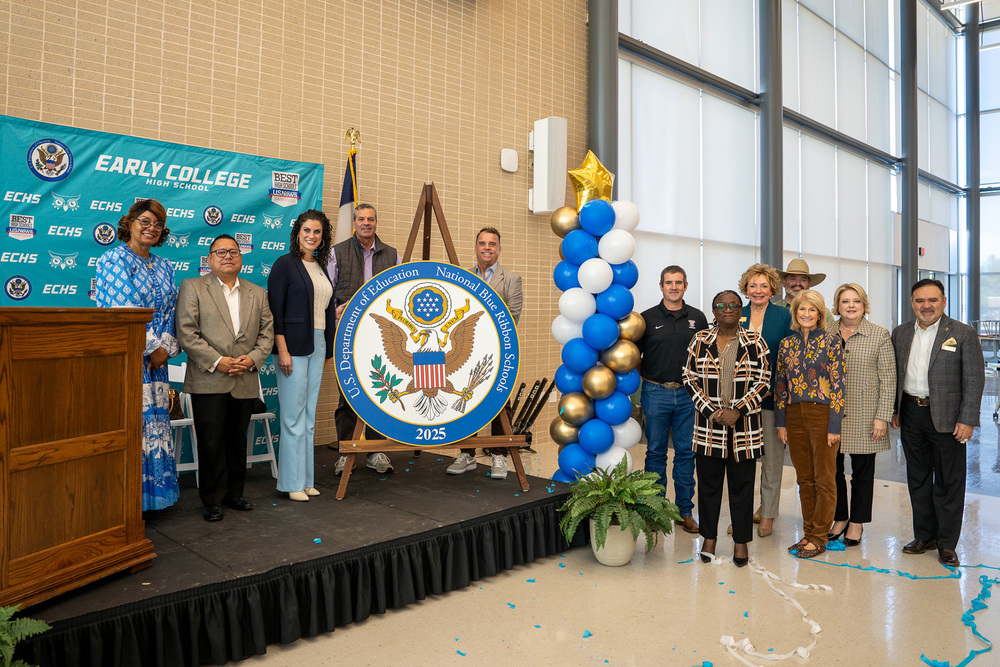 men and women standing near stage with a large blue ribbon schools seal to hang on wall