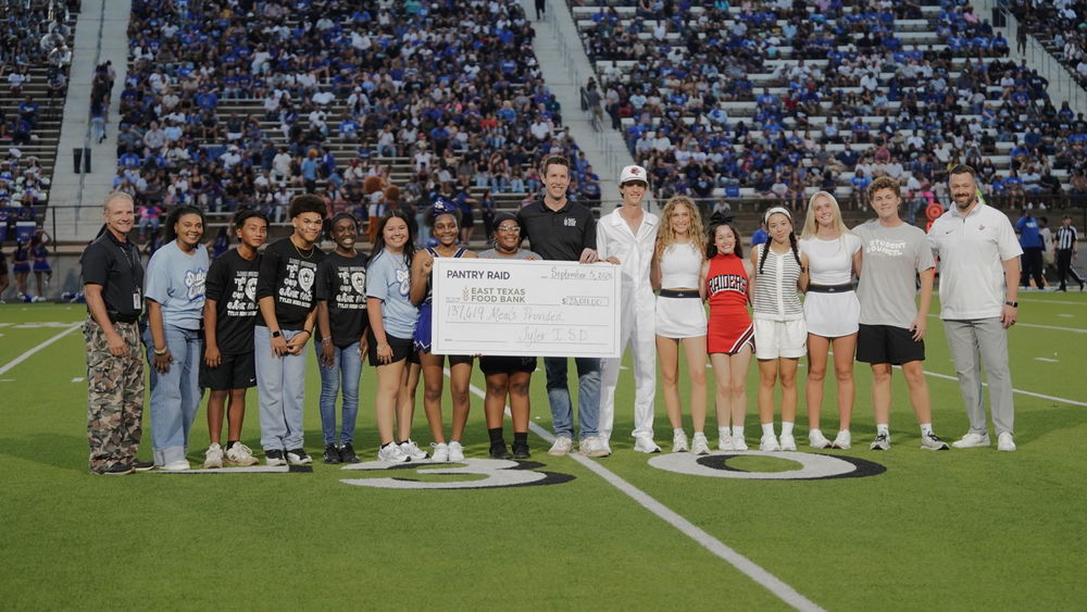 Teens and adults staying on football field holding giant check