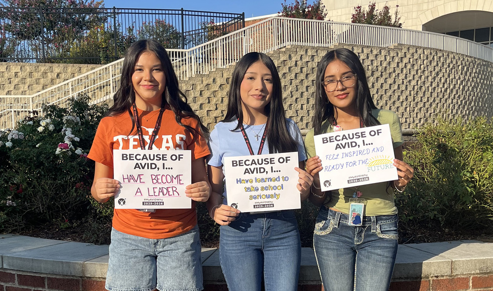 three teen girls holding signs "Because of AVID, I..."