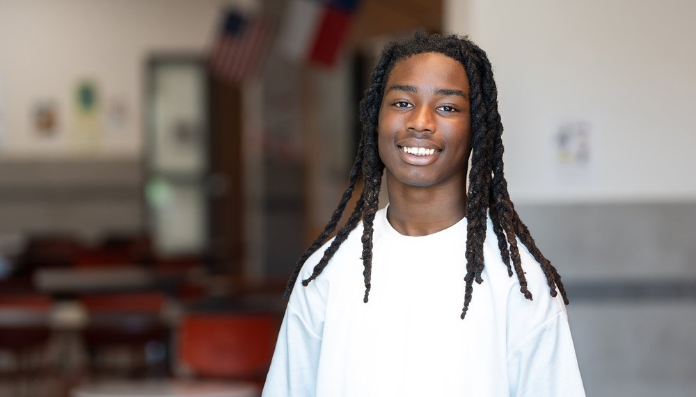 African American teen boy with long braided hair and a white t-shirt in a classroom
