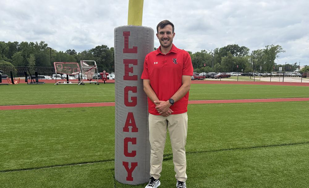 man in red polo and khaki pants standing next to goal post with LEGACY written on it