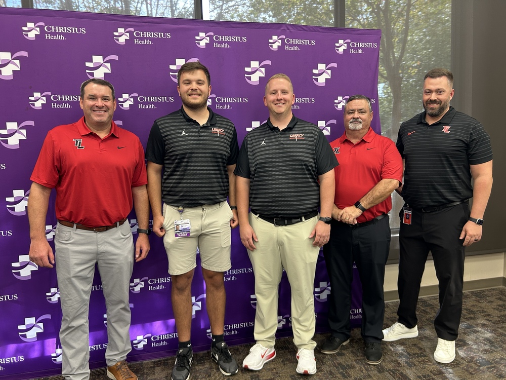 5 men in Tyler Legacy collard shirts standing in front of a CHRISTUS Health backdrop