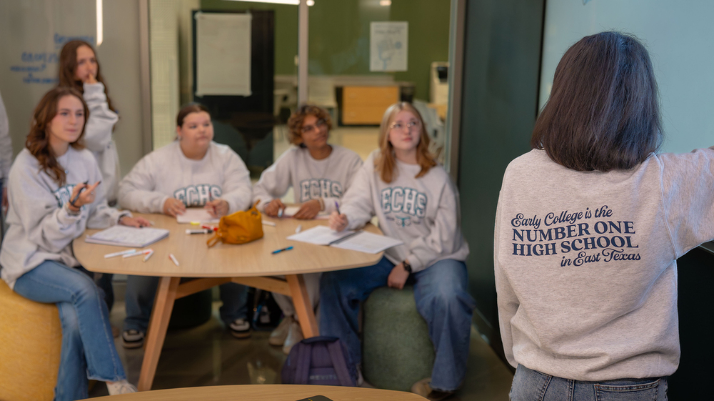teen girls sitting around wood table listening to another teen explain something to them