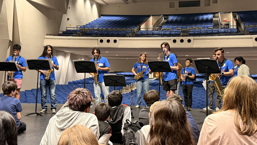 band playing instruments on stage as students sit and watch