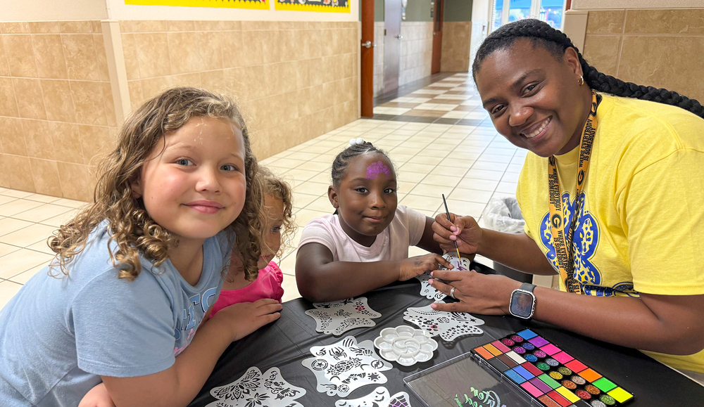 young girls at table picking out design for woman to paint their faces