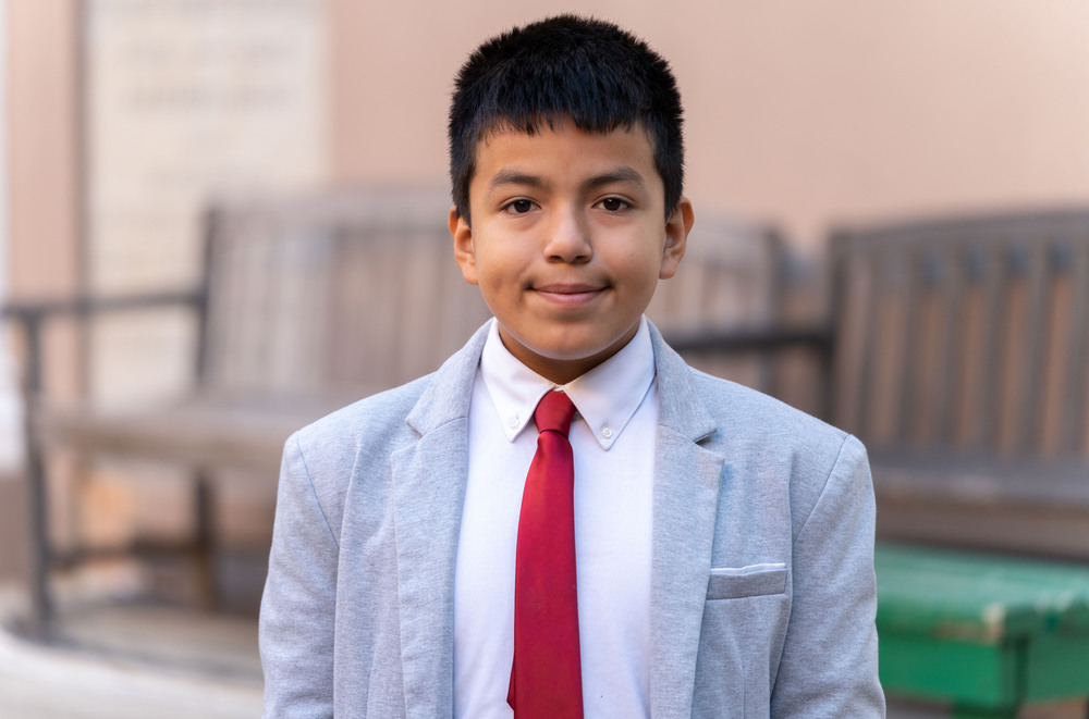 elementary age Hispanic boy wearing suit and tie standing in front of benches