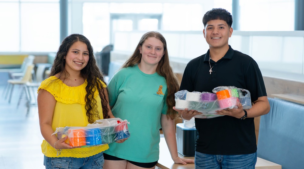 two teen girls and teen boy holding colorful paints in classroom