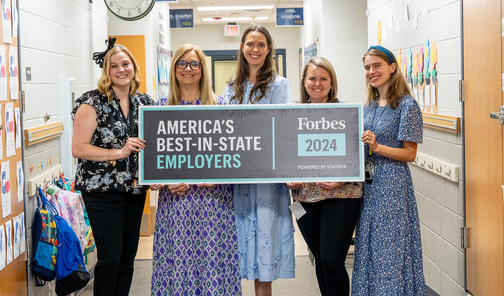 five Caucasian women stand beside each other holding a sign "America's Best-in-State Employers Forbes 2024"