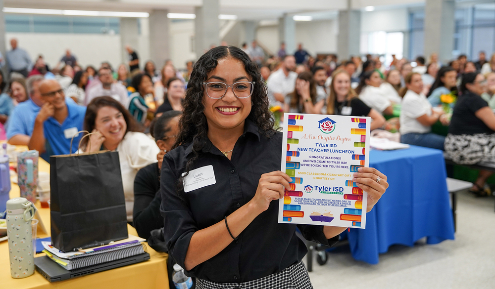 woman holding certificate with room full of people behind her