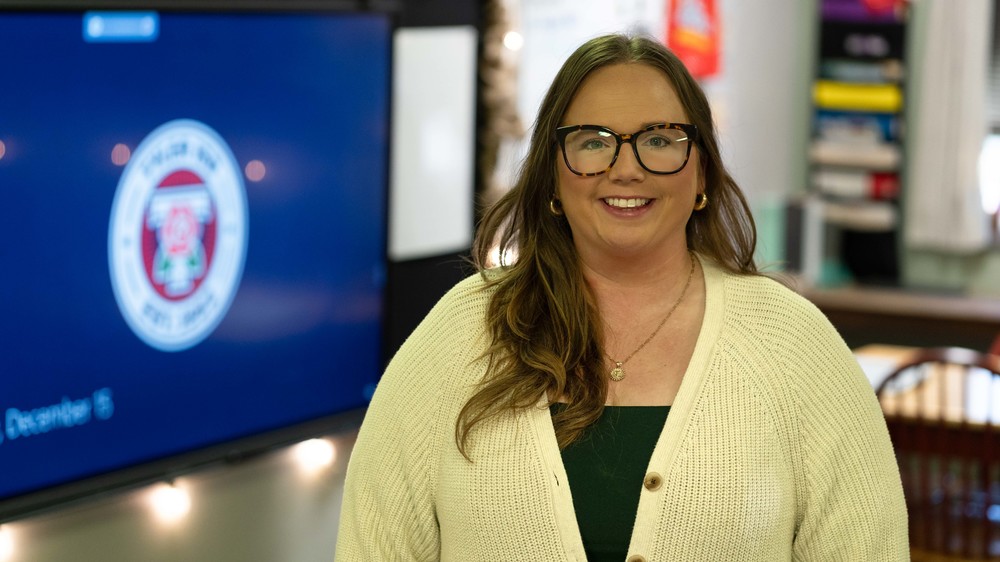 woman with long brown hair and glasses wearing yellow cardigan smiling at the camera