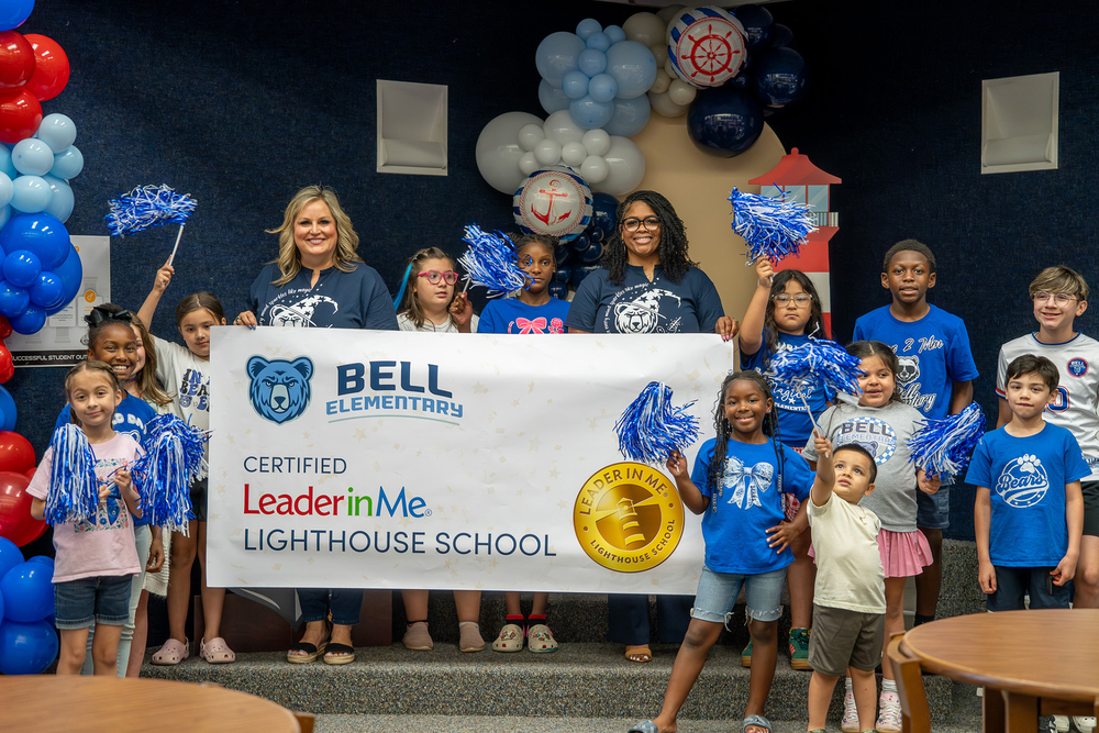 elementary age kids and two women holding a banner with balloons around them. Bell Elementary Certified Leader in Me Lighthouse School