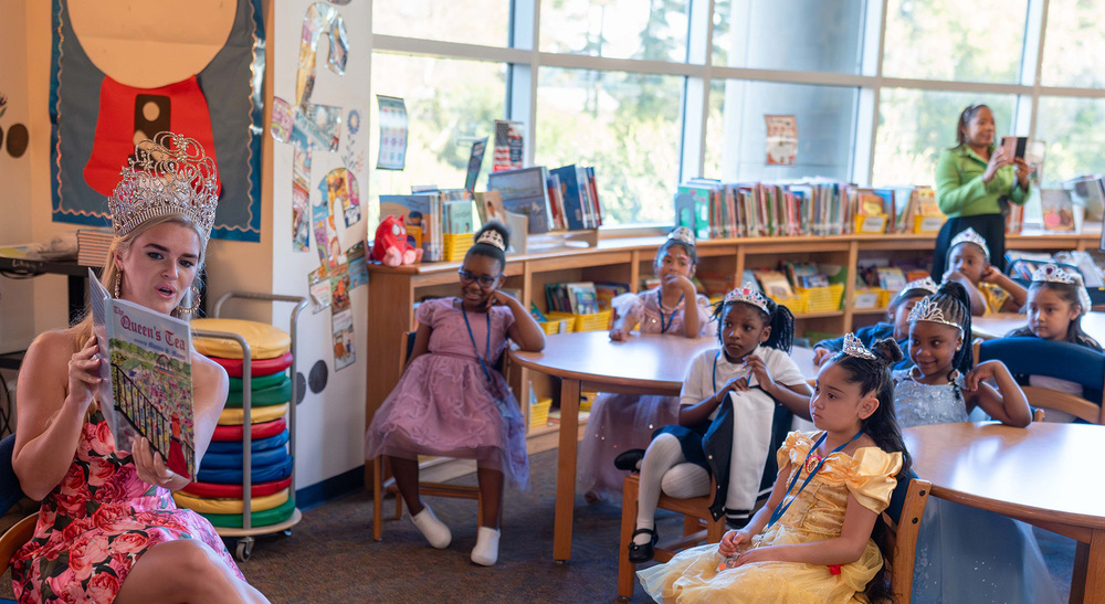 teen girl wearing crown reads book to elementary girls wearing crowns