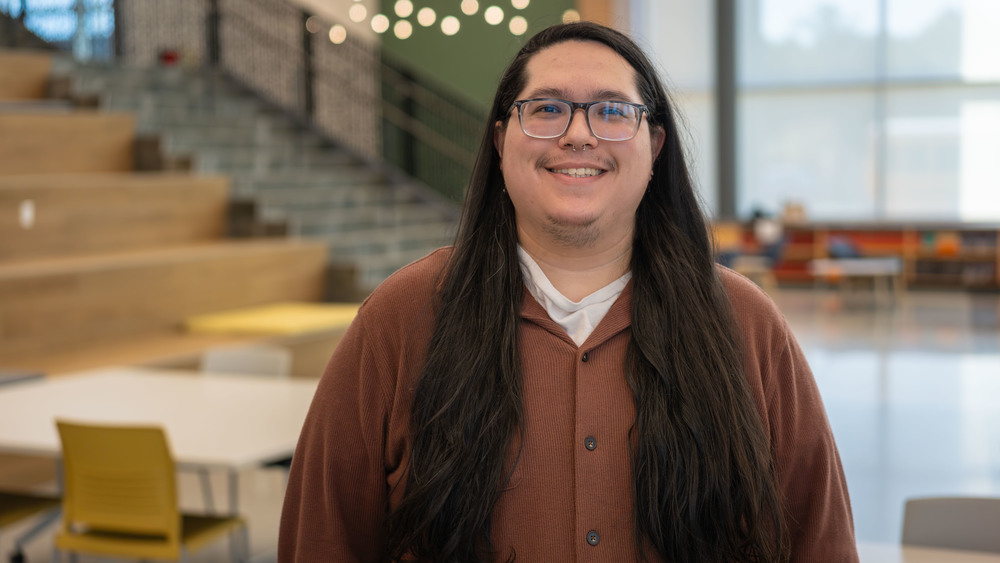 man with long dark hair standing in a classroom