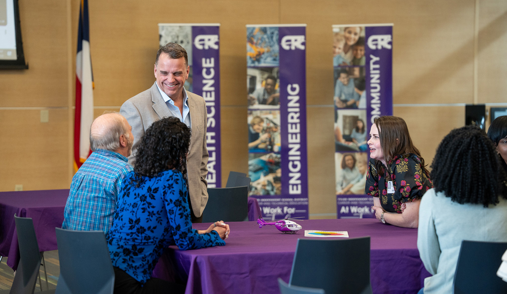 man smiles while talking to men and women at a table