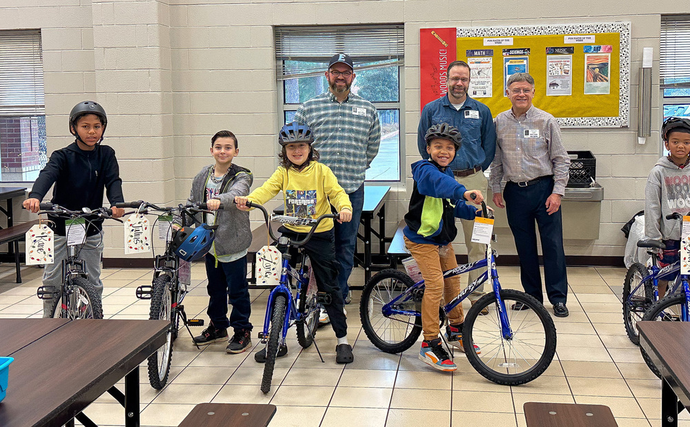 boys on bikes wearing helmets with men standing behind them