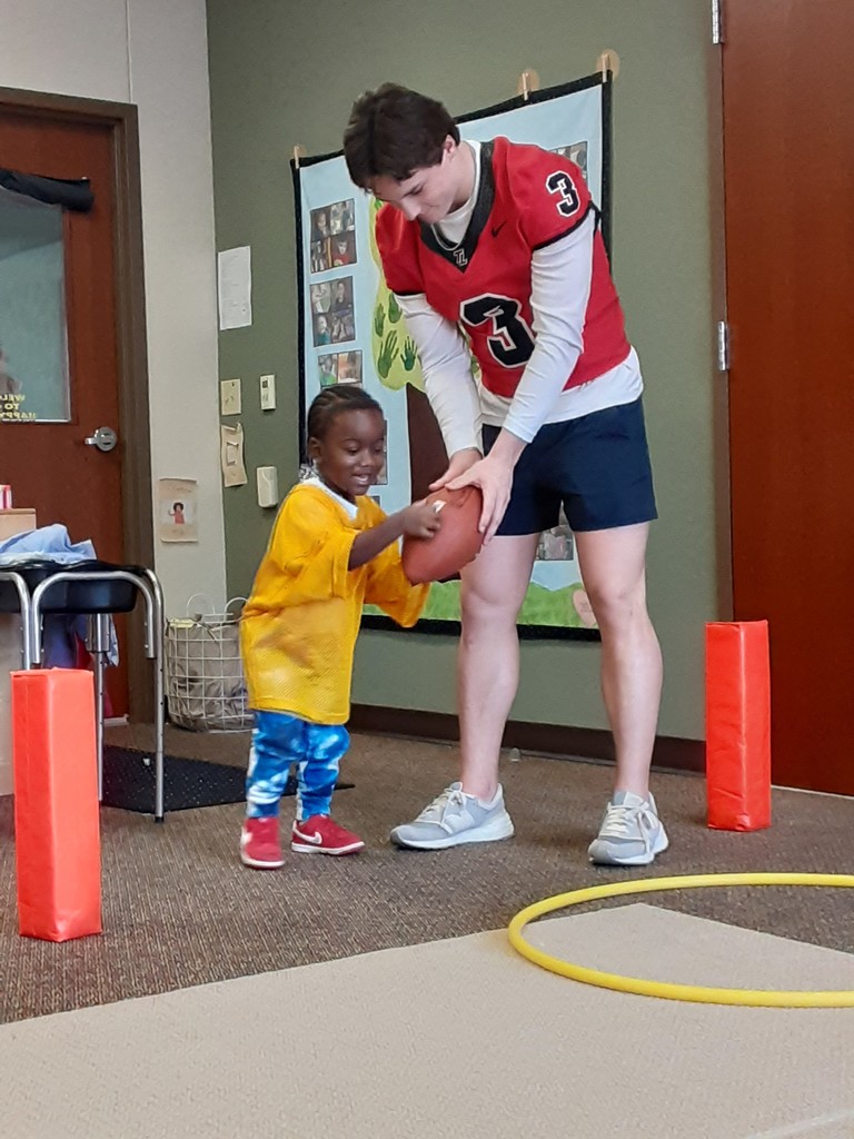 High School Football Players handing a football to a small child