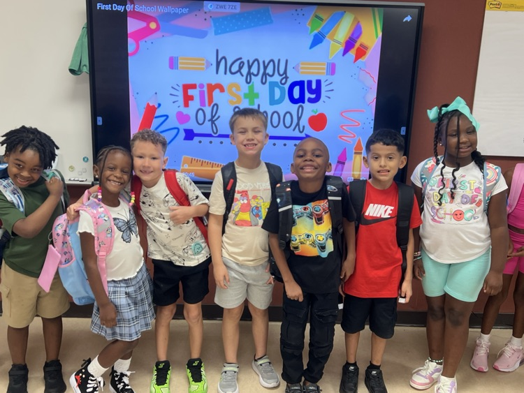 students smiling in front of first day of school poster