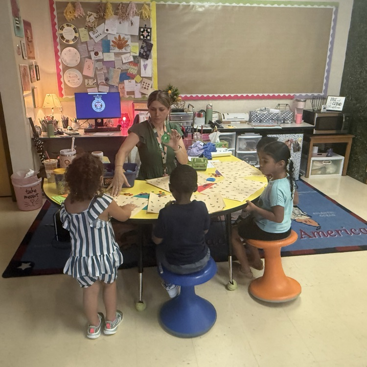 Pre-K students working at teacher table with teacher